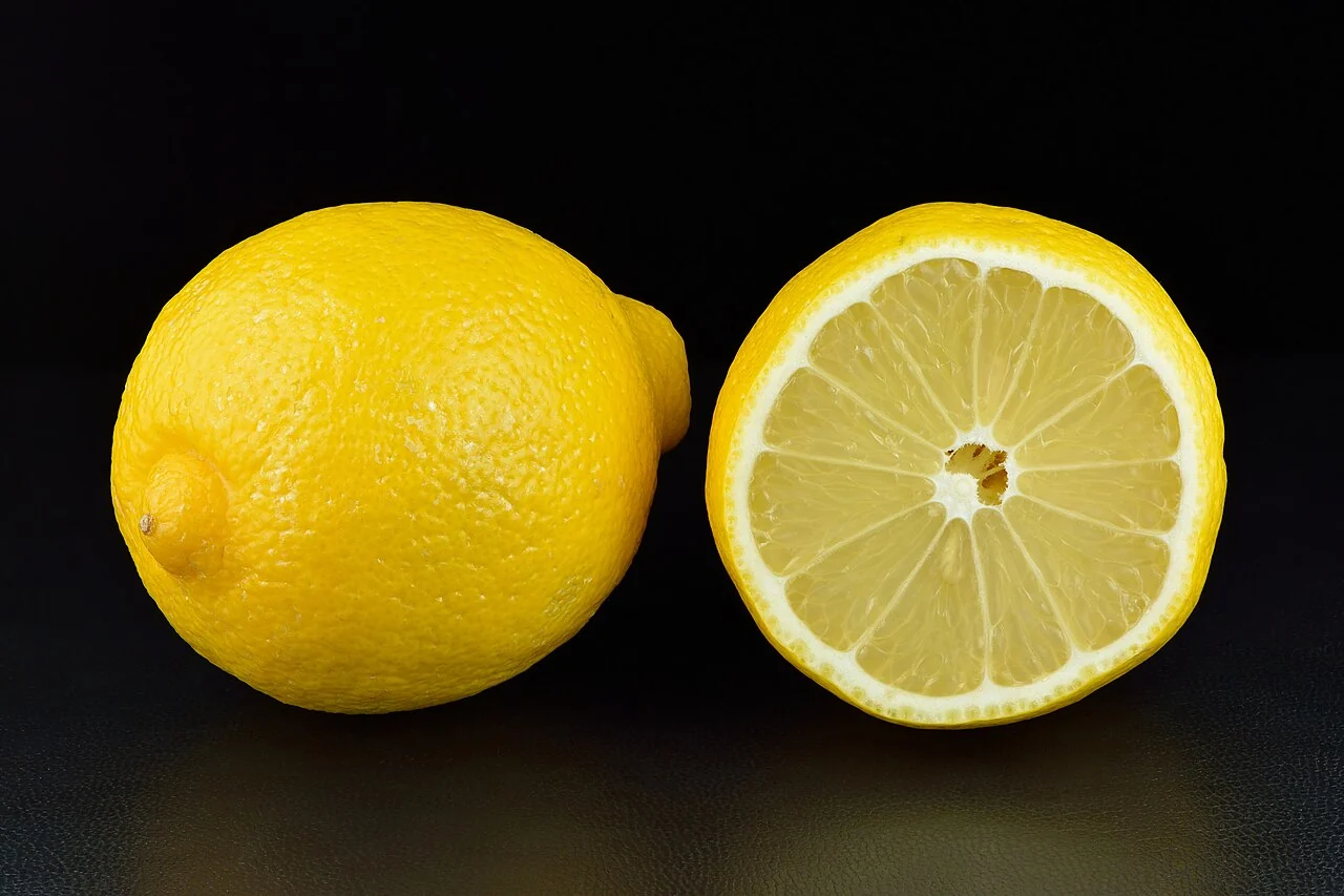 A whole yellow lemon and a halved lemon showing pale citrus segments.