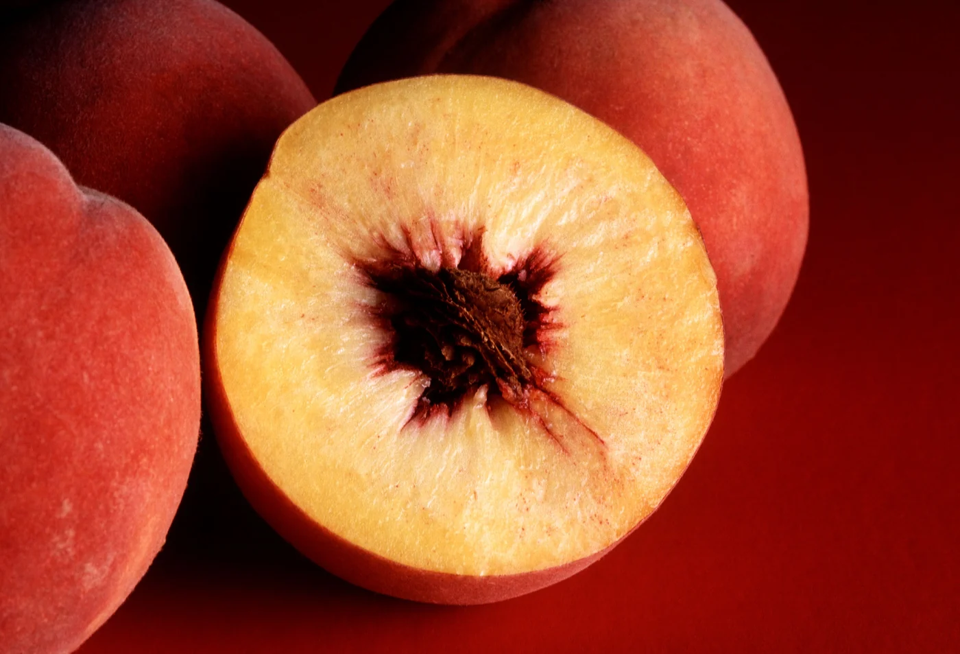 Whole red peaches and a cut peach showing yellow flesh and the central stone cavity.
